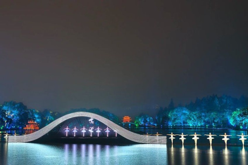 A bridge with illuminated figures, a body of water, and trees in the background. 2