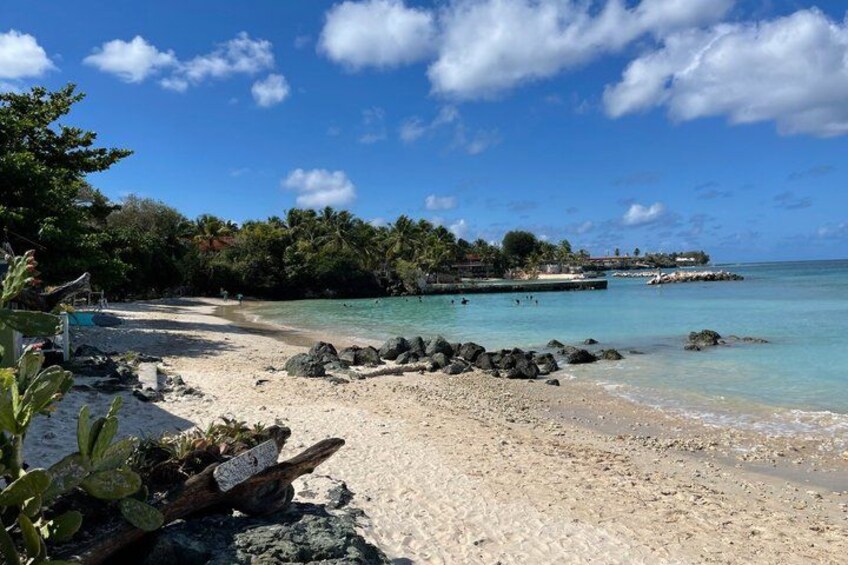 A beach with clear turquoise water, white sand, and rocky outcrops. 2