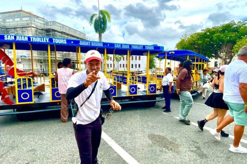 A trolley with 'SAN JUAN TROLLEY TOURS' written on it, people around, and a building in the background. 5