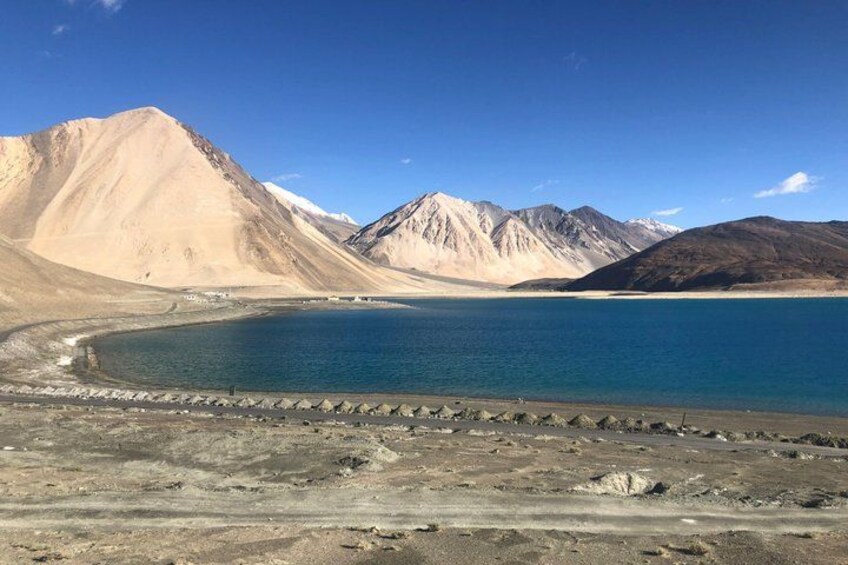 Un lago rodeado de montañas, cielo despejado y una orilla rocosa. 3