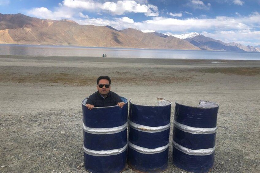 Una persona de pie junto a tres barriles grandes en un paisaje árido con montañas al fondo. 4