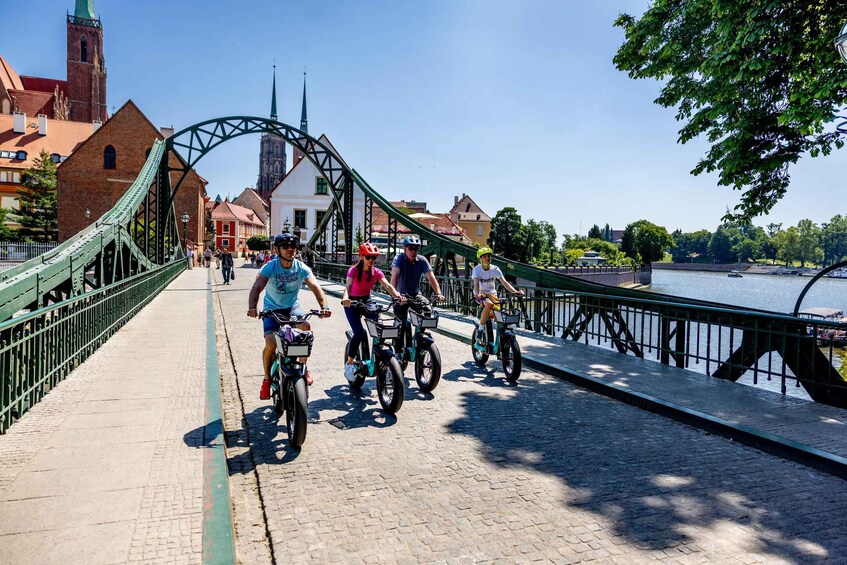People riding bicycles on a bridge with a river and buildings in the background. 5