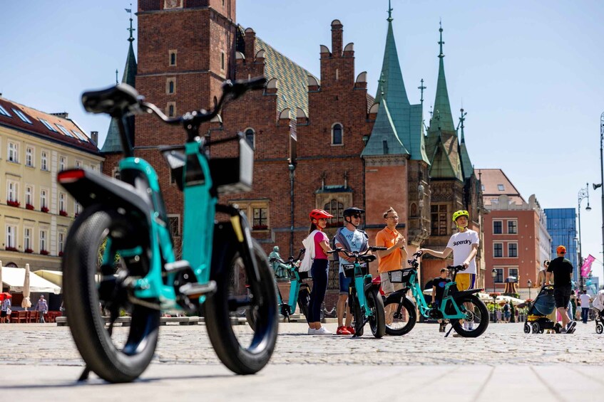 A group of people with bicycles in a public square with historic buildings in the background. 4