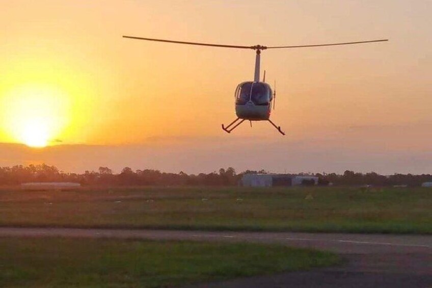 A helicopter flying over a field during sunset. 2
