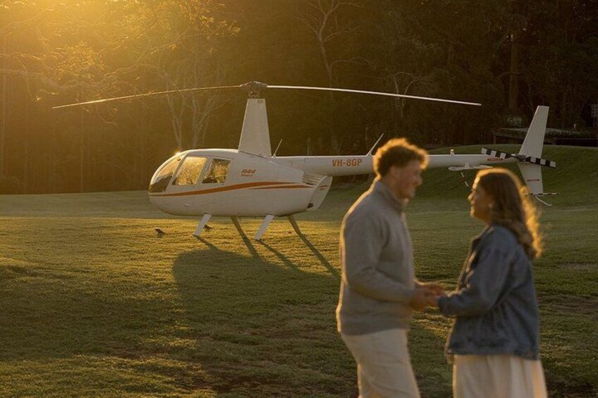 A helicopter with registration VH-8GP parked on a grassy field during sunset. 3
