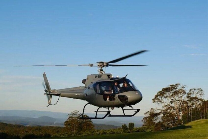 A helicopter with the registration VH-EOP flying over a hilly landscape with trees and a clear sky. 1