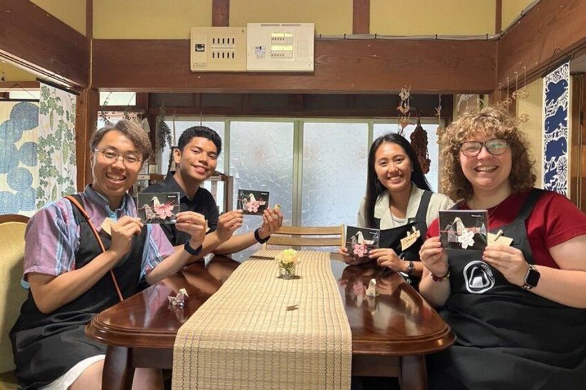 Four people sitting at a wooden table with a woven tablecloth, holding cards with images on them. 5