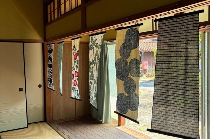A traditional Japanese room with tatami flooring, sliding doors, and various hanging textiles. 4