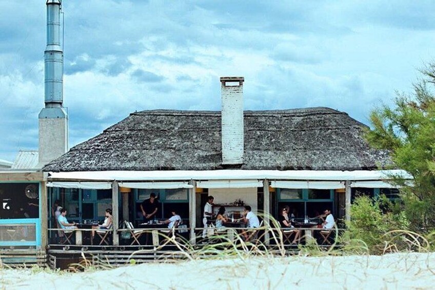 A building with a thatched roof and a chimney, surrounded by people sitting at tables. 1