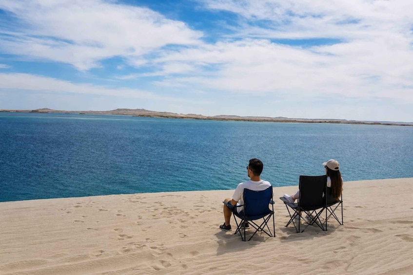 Two people sitting on beach chairs facing a calm sea with a clear sky. 4