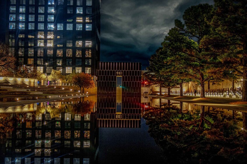 A nighttime cityscape with a modern building reflecting in a body of water, surrounded by trees and illuminated windows. 5