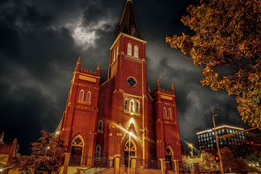 A large, red-brick church with a tall steeple and multiple towers, illuminated at night. 1