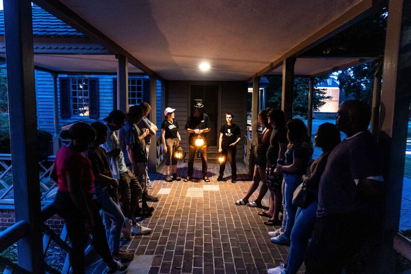 A group of people gathered around a person holding a lantern in a covered outdoor area with brick flooring. 2