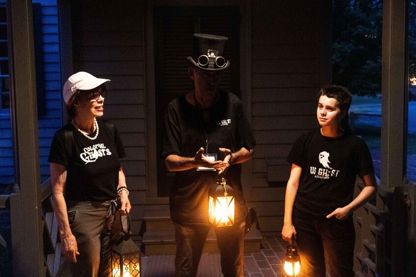 Three people standing on a porch with a lit lantern. 4