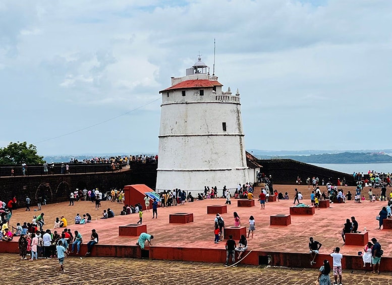 A historic lighthouse with a red roof, surrounded by a large crowd of people. 1