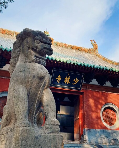 A stone lion statue in front of a traditional Chinese building with a tiled roof and a sign with Chinese characters. 1