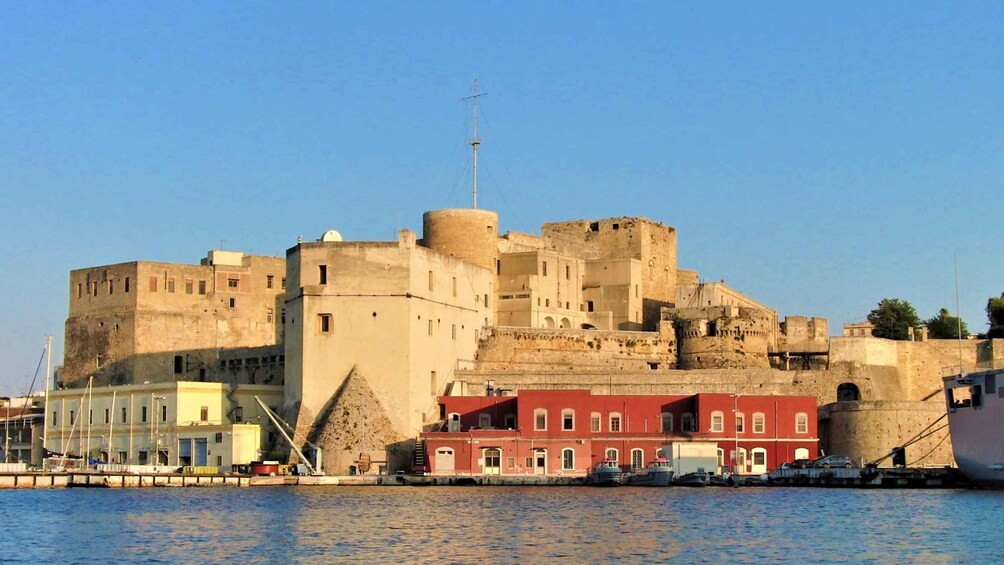 A coastal city with a historic fortification, a modern red building, and a clear blue sky. 3