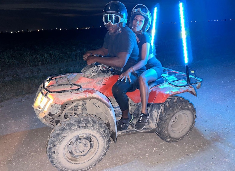 Two people on a red ATV at night with a blue light on the back. 3