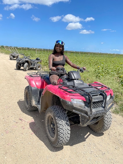 A person on a red ATV in a field with another ATV in the background. 1