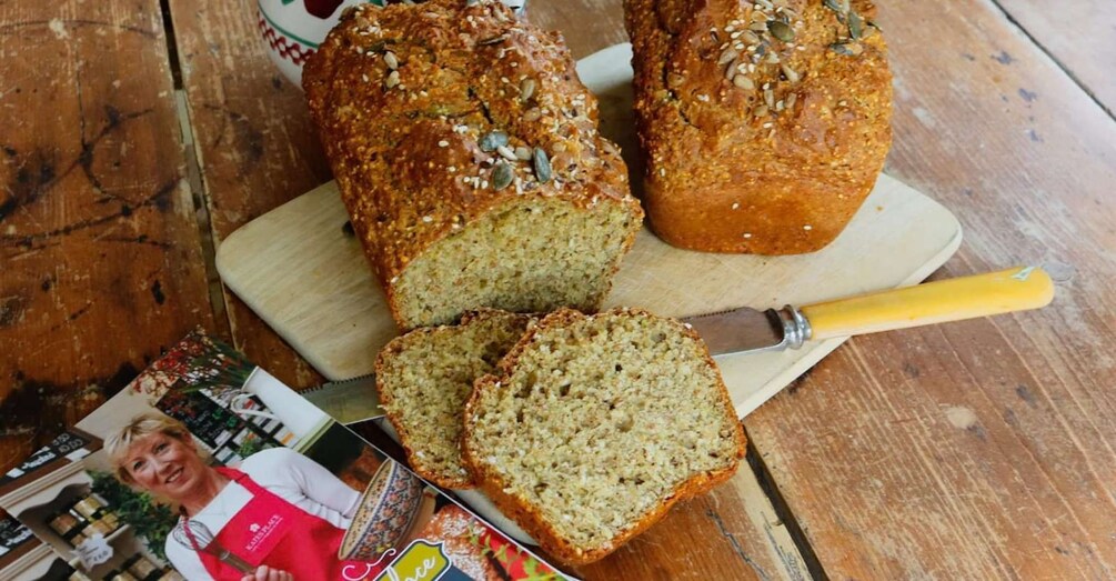 A loaf of seeded bread on a wooden cutting board with a knife, and a magazine with a woman's photo on it. 3