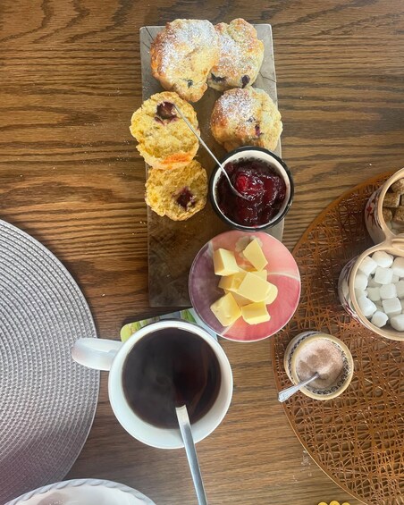 A wooden table with pastries, a cup of coffee, and condiments. 1