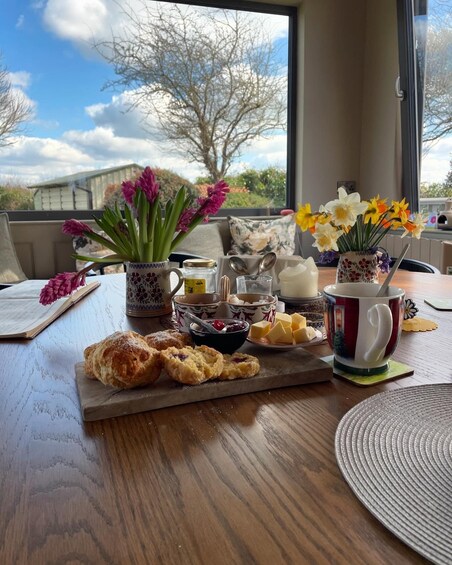 A breakfast setting with pastries, flowers, and a view of trees and buildings. 4