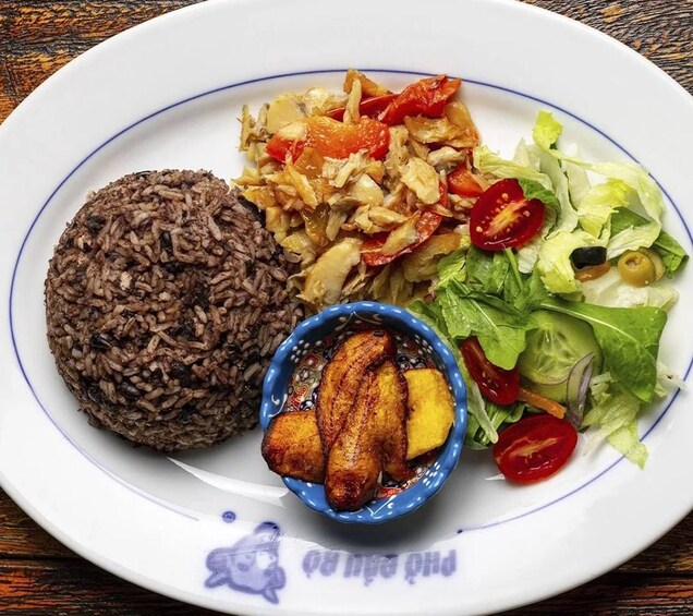 Une assiette contenant du riz noir, des bananes plantains frites, une salade de légumes et un petit bol de bananes plantains frites. 1