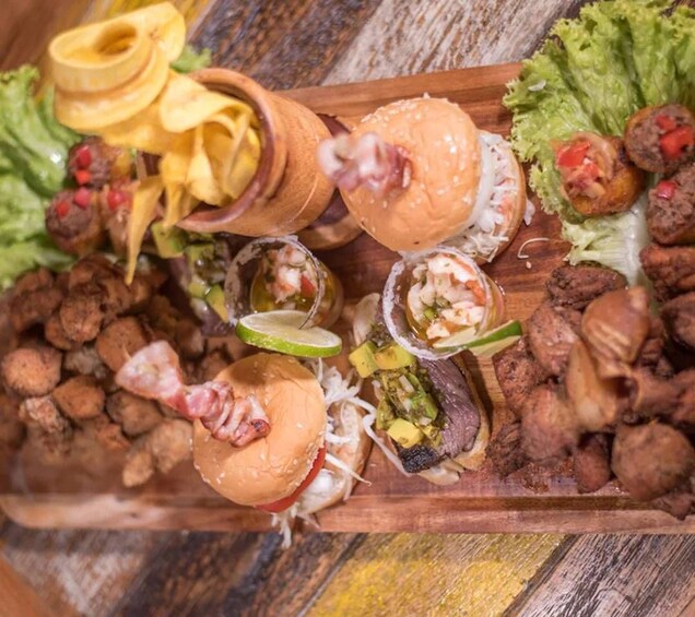 Un plateau en bois contenant divers aliments, notamment des hamburgers, des tacos et un assortiment d’accompagnements. 5