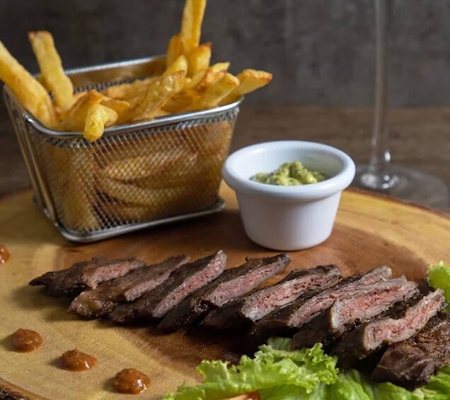 Une planche à découper en bois sur laquelle on a posé des tranches de steak, un panier de frites et un petit bol de sauce. 2