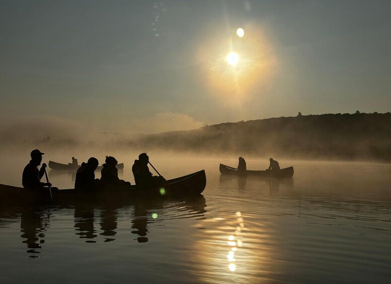 People in canoes on a calm body of water with the sun low on the horizon, creating a silhouette effect. 2