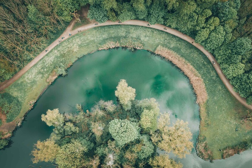 Eine Vogelperspektive auf einen kreisrunden See, umgeben von dichtem Wald, mit einem gewundenen Pfad entlang des Ufers. 3