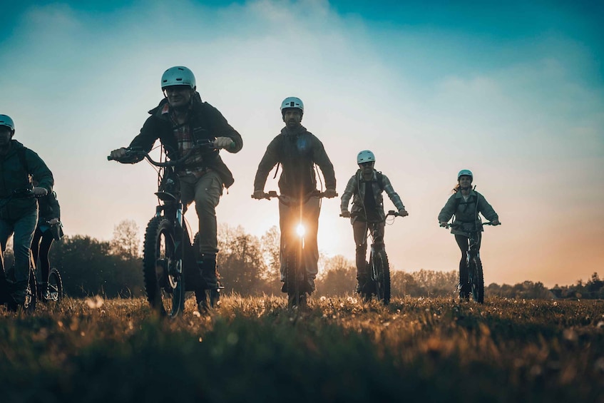 Eine Gruppe von Mountainbikern in einem Feld, im Hintergrund geht die Sonne unter. 2