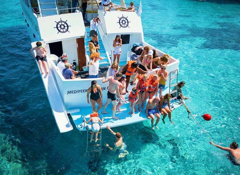A group of people on a boat with clear blue water, wearing life jackets, and some are swimming. 3