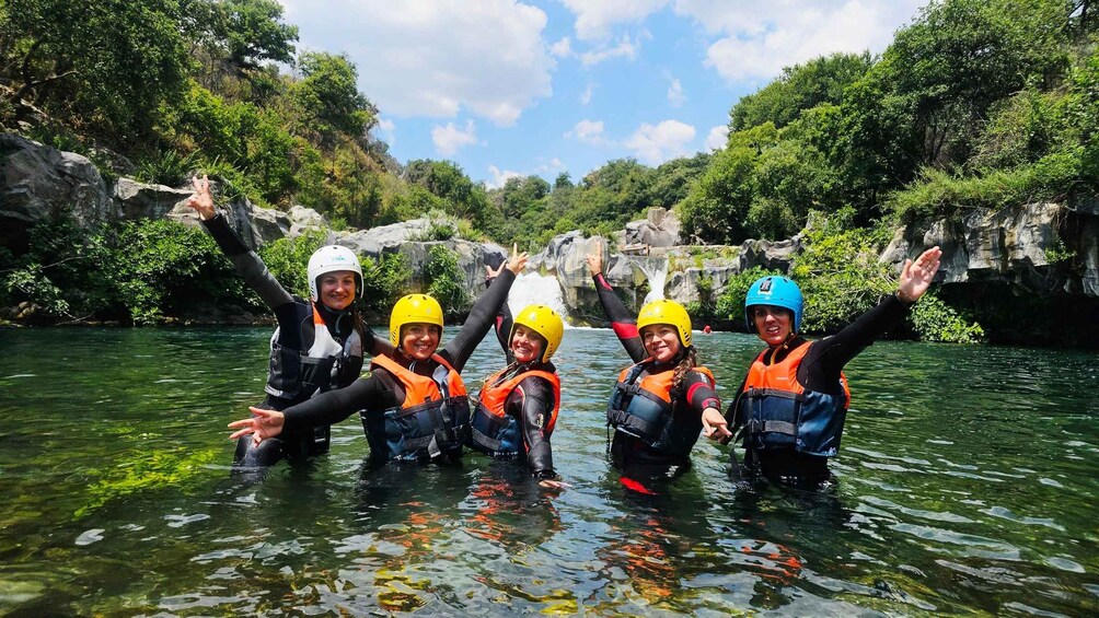 Un grupo de personas en un río, usando cascos y chalecos salvavidas, rodeado de vegetación y acantilados rocosos. 1