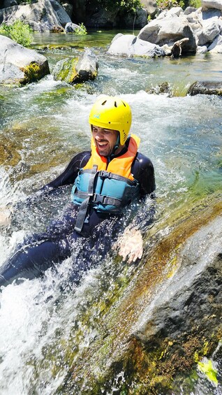 Una persona con traje de neopreno y casco amarillo recorre un río de aguas cristalinas y rocas. 5