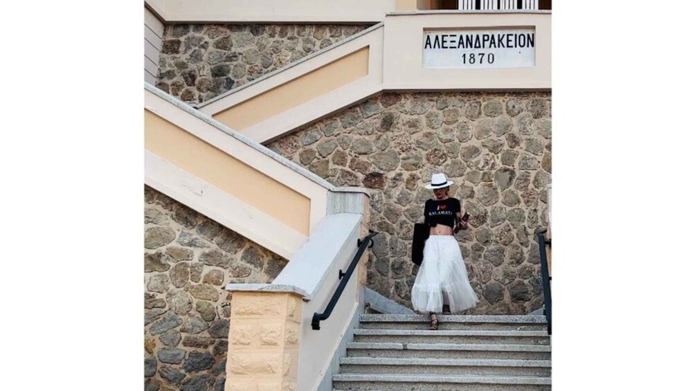 A person descending a stone staircase with a sign reading 'AAEANAPAKEION 1870' above. 2