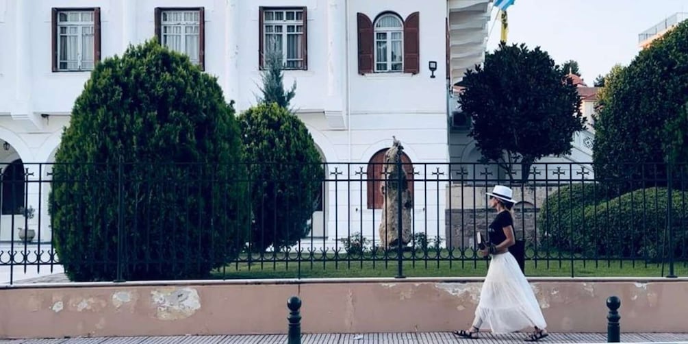 A woman walking along a fence with a building in the background. 3