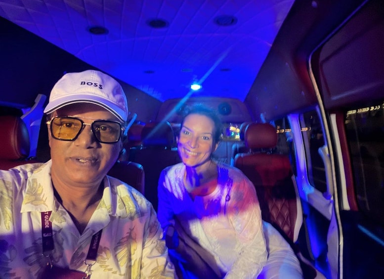 Two people seated in a vehicle with red seats and a blue-lit ceiling. 3