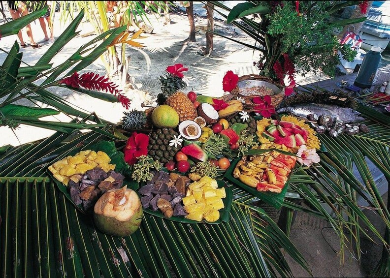 Exhibición de frutas y verduras tropicales sobre un tapete de hojas de palma, con diversas frutas, verduras y flores. 3
