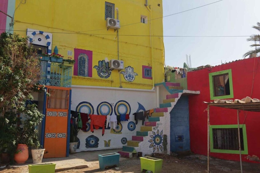 Un bâtiment aux couleurs vives, orné d’une fresque murale, avec un petit jardin et une structure rouge. 5