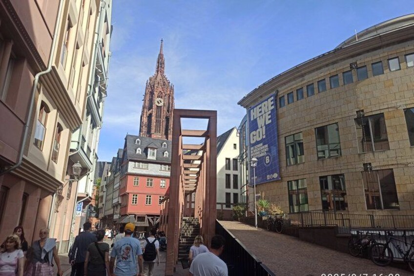 A street with historic buildings, a tall church spire, and a blue banner. 5