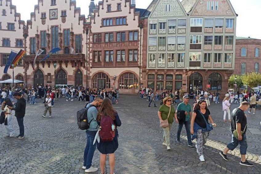 A cobblestone square with historic buildings, tourists, and a clear sky. 1