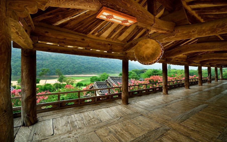 A wooden pavilion with a view of traditional architecture and a garden with pink flowers. 4