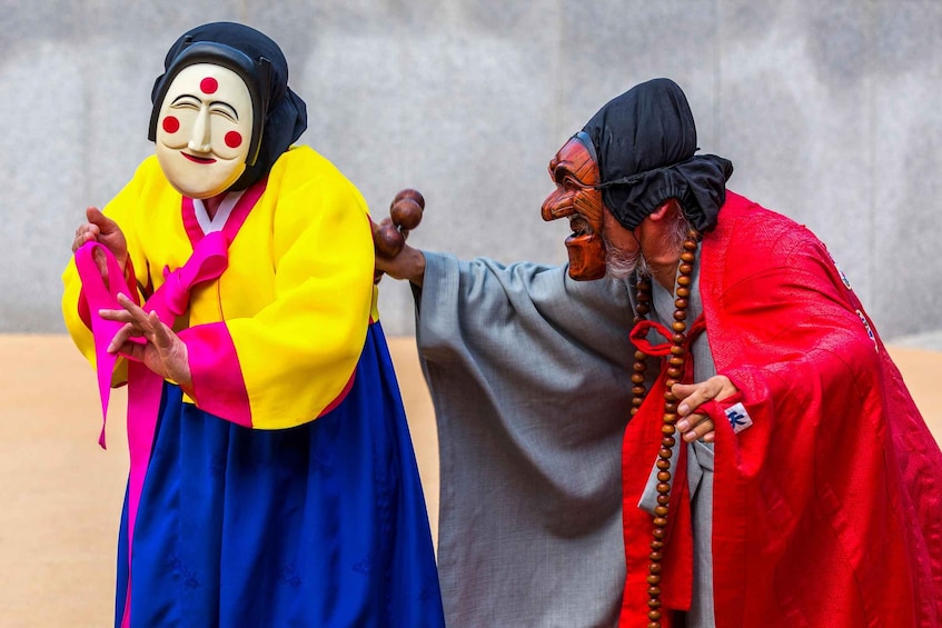 Two individuals in traditional attire, one with a colorful robe and the other with a red robe and beaded necklace. 1