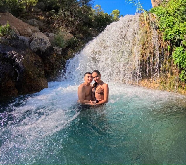 Two people in a natural water body with a waterfall. 4