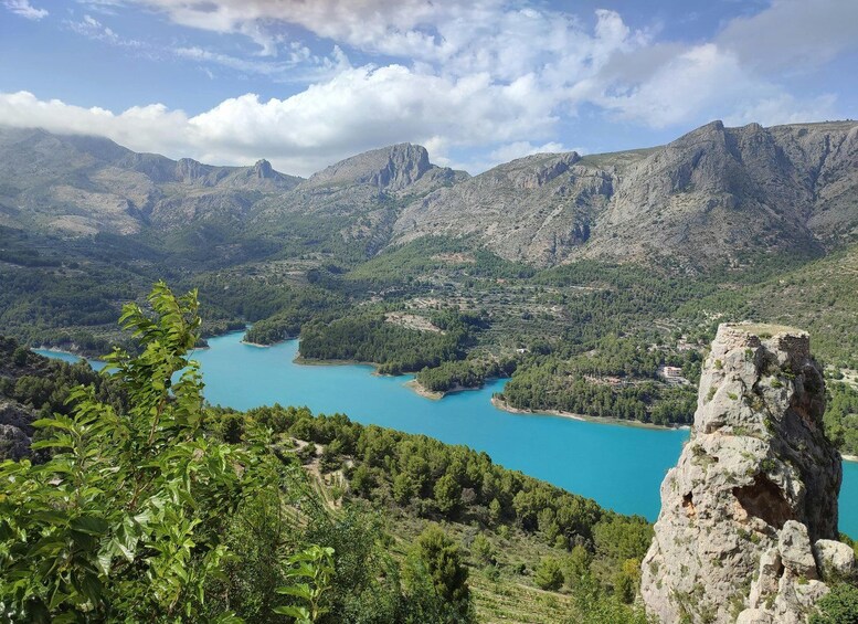 A mountainous landscape with a turquoise lake surrounded by greenery and rocky outcrops. 2
