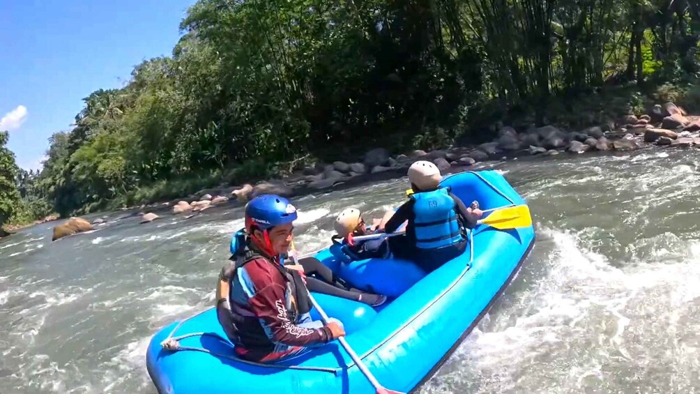 A blue inflatable raft with two people paddling on a river surrounded by rocks and greenery. 5