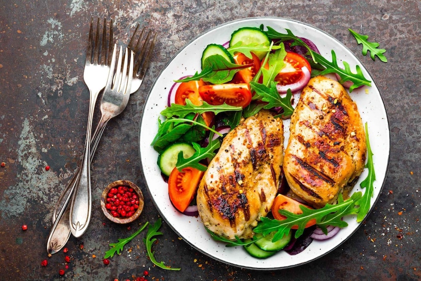 A plate of grilled chicken with vegetables and a small bowl of red berries. 4