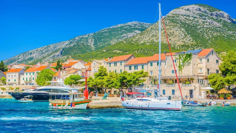A coastal town with boats docked, buildings with red roofs, and a mountainous backdrop. 3