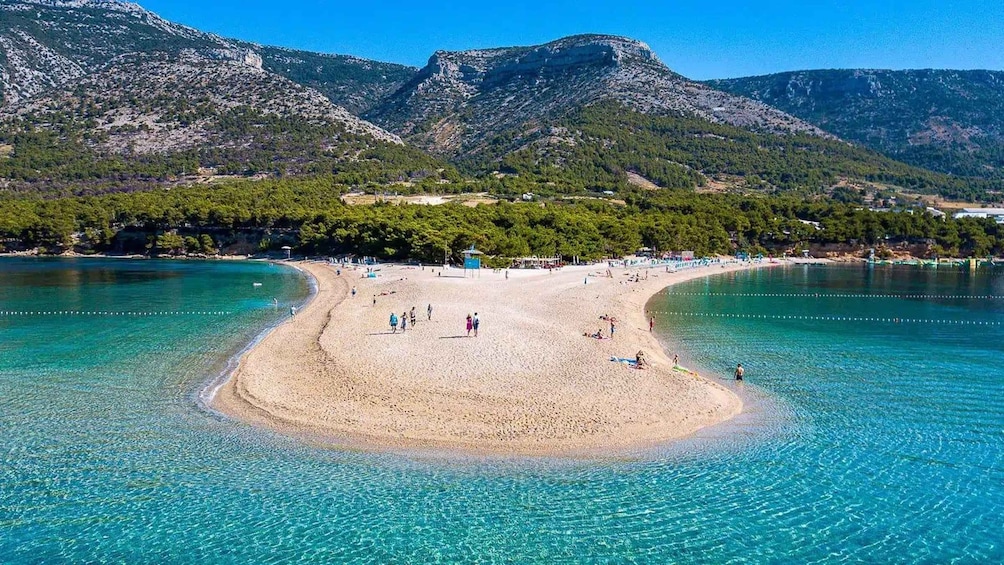 A beach with clear turquoise water, surrounded by mountains and trees. 2